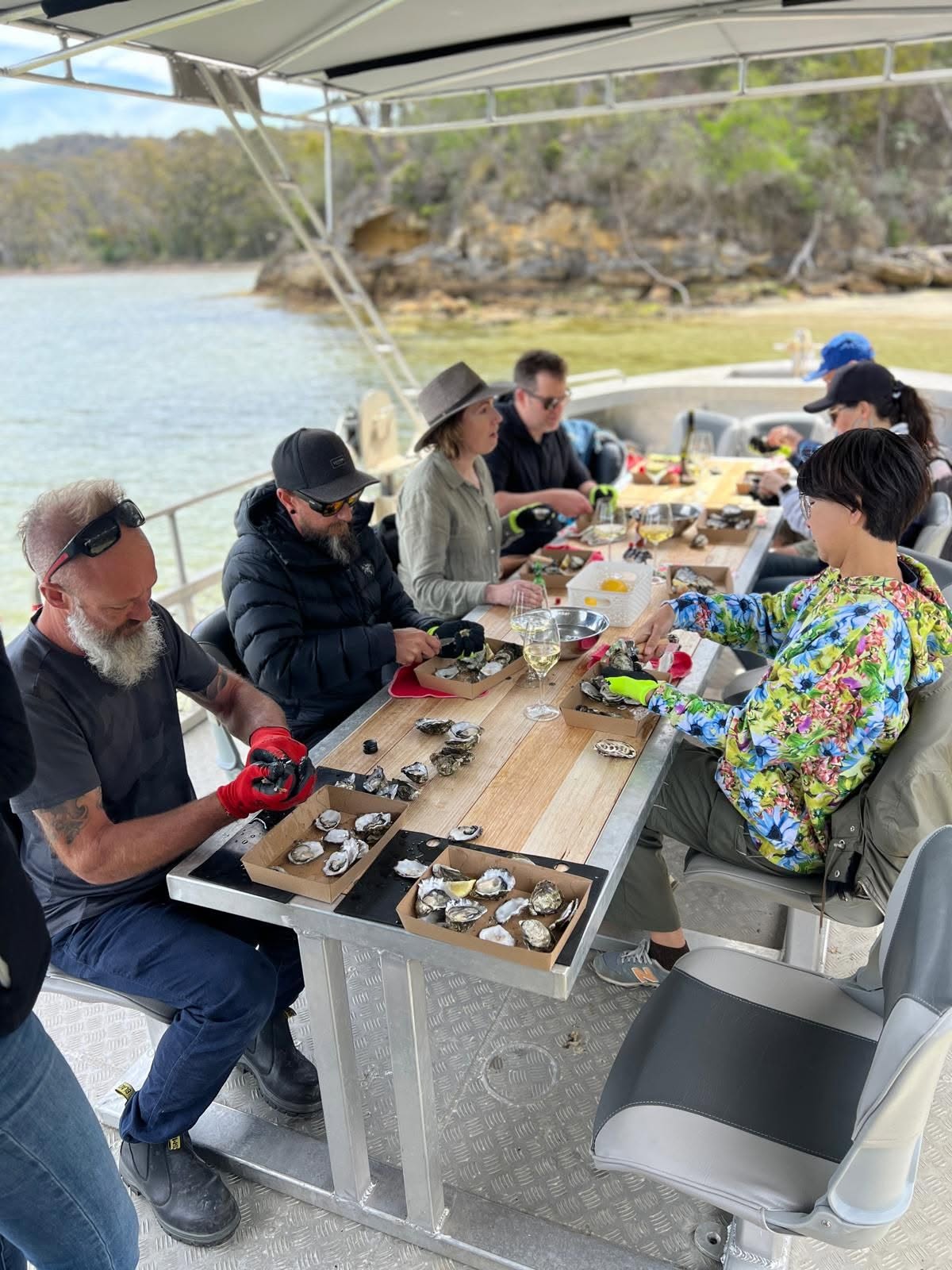 Guests shucking and eating oysters around the timber table on board